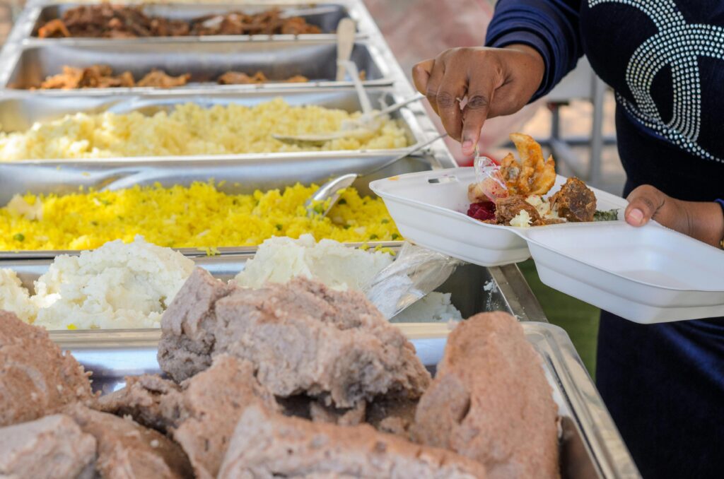 pexels photo 12253095 12253095 A person serves a variety of foods from a buffet station onto their plate.